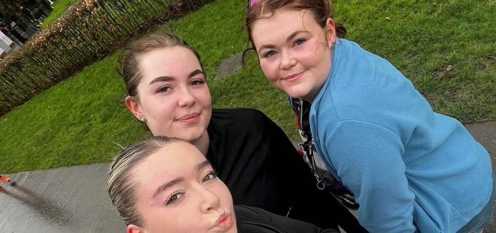 Mia Rose Howard, Masie Cupit and Olivia Cupit are standing in a park, smiling at the camera wearing their running attire.